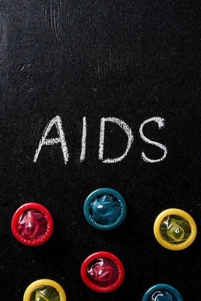 Top view of aids sign with multicolored condoms on black background — Stock Photo