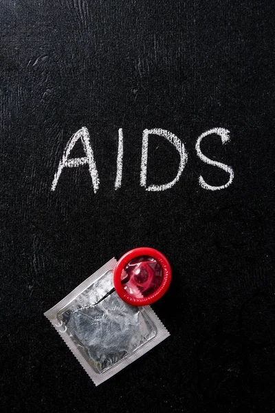 Top view of aids sign and red condom with silver packaging on black background — Stock Photo