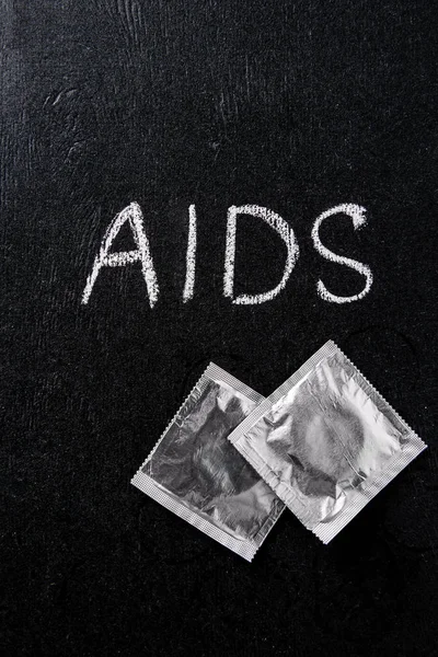 Vista superior do sinal de aids e preservativos de prata no fundo preto — Fotografia de Stock