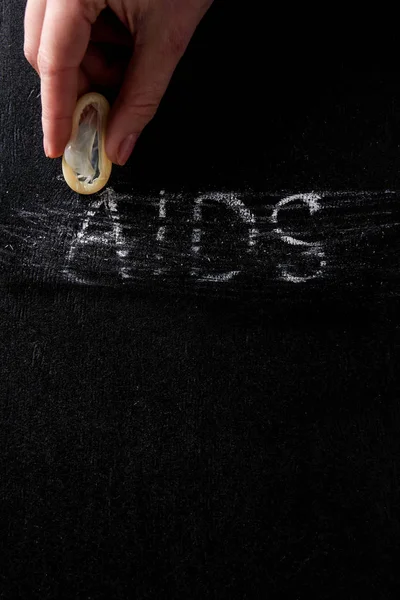 Top view female hand holding condom with aids sign on black background — Stock Photo