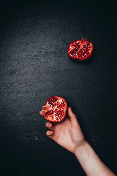 Partial view of female hand and cut pomegranate on black tabletop — Stock Photo