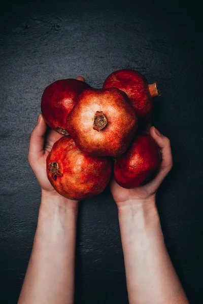 Cropped shot of woman holding ripe garnets in hands on black surface — Stock Photo