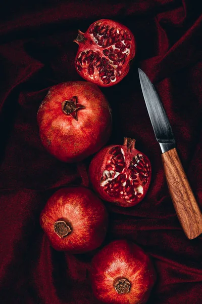 Flat lay com granadas frescas e faca em fundo de tecido de veludo vermelho — Fotografia de Stock