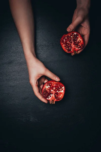 Partial view of woman holding garnets halves in hands on black surface — Stock Photo