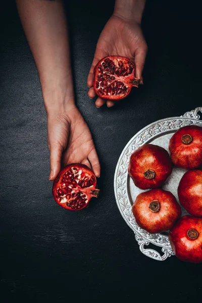 Partial view of woman holding pomegranate halves on black surface with metal tray — Stock Photo