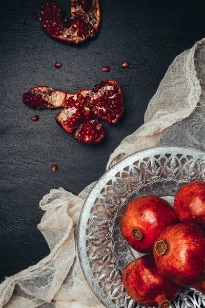 Essenszusammensetzung mit reifen und frischen Granatäpfeln, Metallschale und Gaze auf schwarzer Tischplatte — Stockfoto