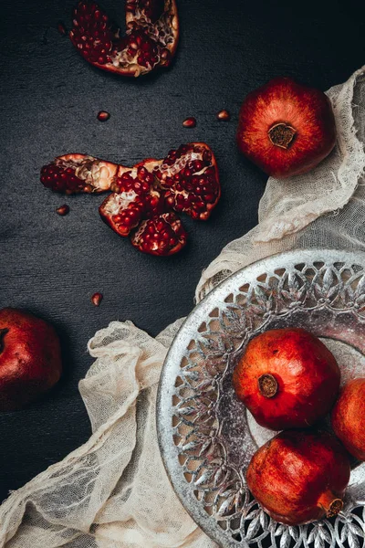 Food composition with ripe and fresh pomegranates, metal bowl and gauze on black tabletop — Stock Photo