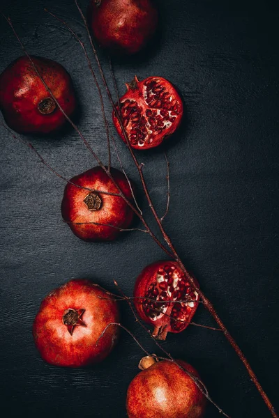 Top view of ripe pomegranates and twig arrangement on black surface — Stock Photo