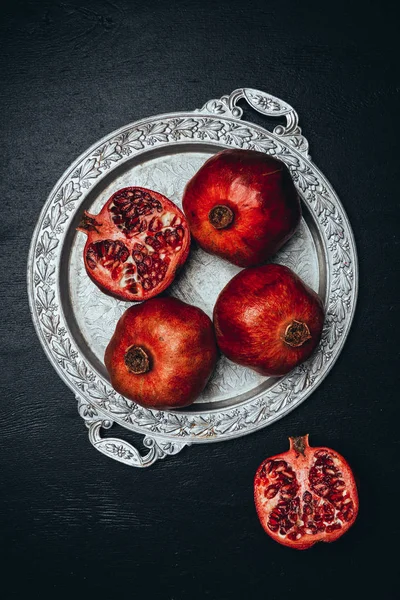 Flat lay with fresh pomegranates on metal serving tray on black tabletop — Stock Photo