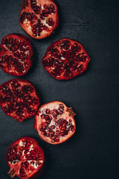 Top view of cut pomegranates halves arrangement on black surface — Stock Photo