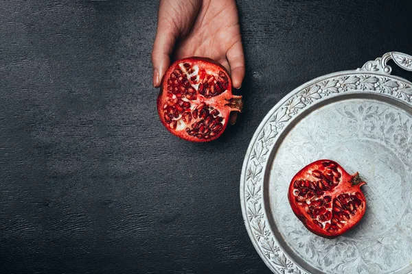 Partial view of woman holding half of garnet in hand on black surface with metal serving tray — Stock Photo