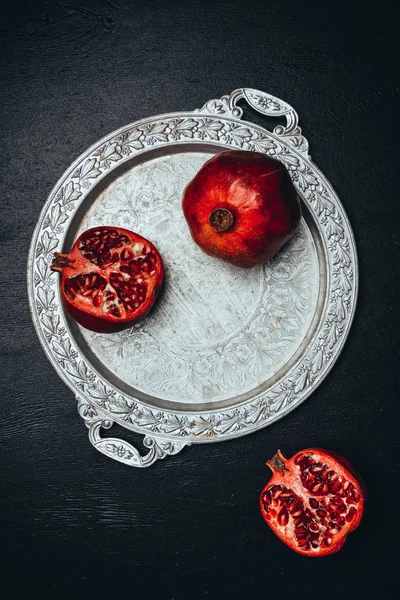 Flat lay with fresh pomegranates on metal serving tray on black tabletop — Stock Photo