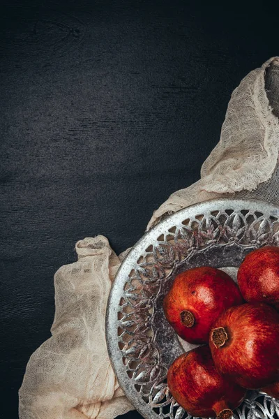 Food composition with ripe and fresh pomegranates, metal bowl and gauze on black tabletop — Stock Photo