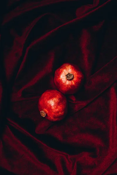 Vista superior de romãs maduras em pano de fundo de tecido de veludo vermelho — Fotografia de Stock