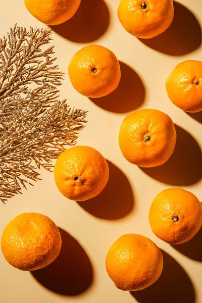 Puesta plana con mandarinas saludables y ramita decorativa dorada sobre fondo beige - foto de stock