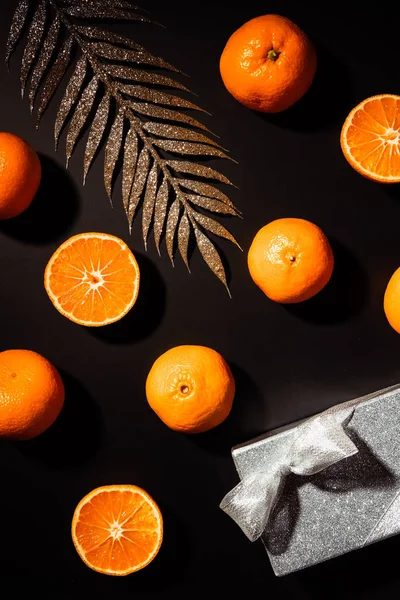 Vista superior de tangerinas frescas, galho decorativo e caixa de presente sobre fundo preto — Fotografia de Stock