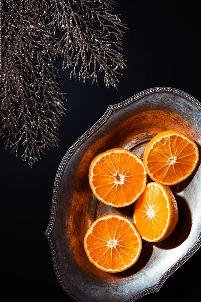 Flat lay with mandarins in metal bowl and decorative silver twig on black backdrop — Stock Photo