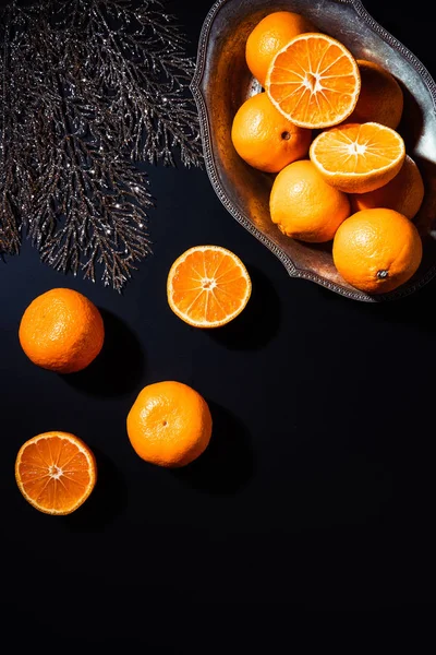 Flat lay com tangerinas, galho de prata decorativo e tigela de metal no fundo preto — Fotografia de Stock