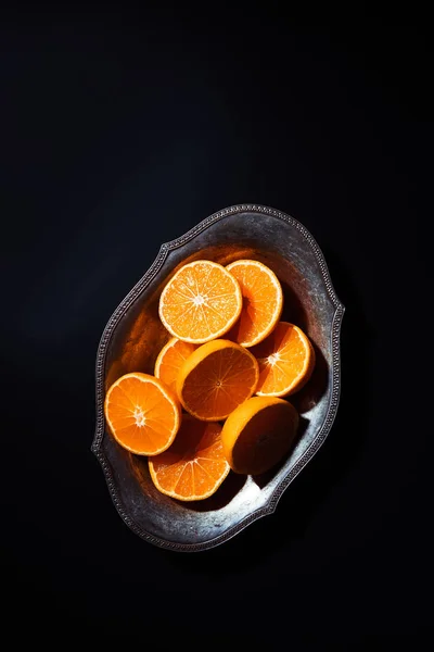 Top view of cut mandarins halves in metal bowl on black tabletop — Stock Photo