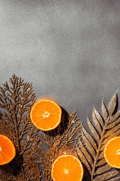 Tendido plano con mandarinas frescas y ramitas decorativas doradas sobre fondo gris - foto de stock