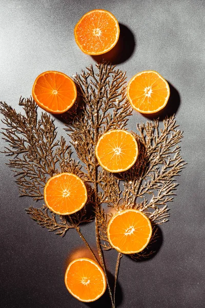 Flat lay with arranged mandarins halves and golden twig on grey backdrop — Stock Photo