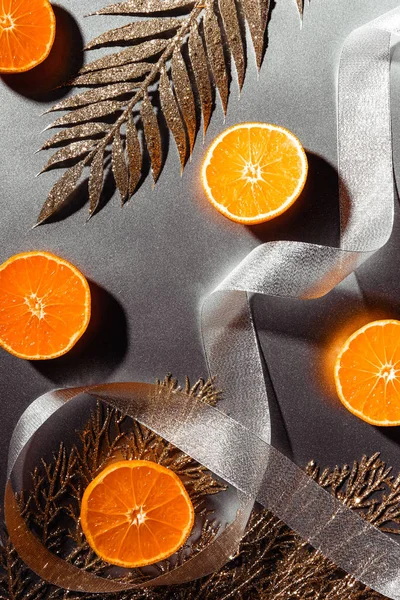 Deitado com tangerinas frescas, fita de prata e galhos dourados decorativos em fundo cinza — Fotografia de Stock