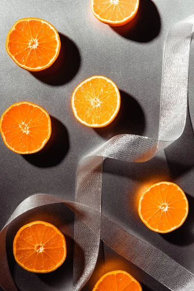 Flat lay with arranged mandarins halves with silver ribbon on grey backdrop — Stock Photo