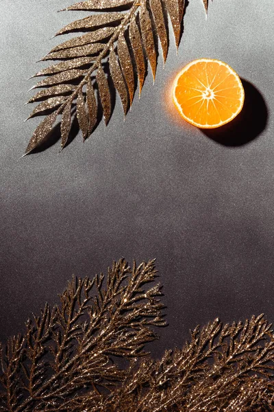 Vue de dessus de la moitié de mandarine coupée et des brindilles dorées décoratives sur fond gris — Photo de stock