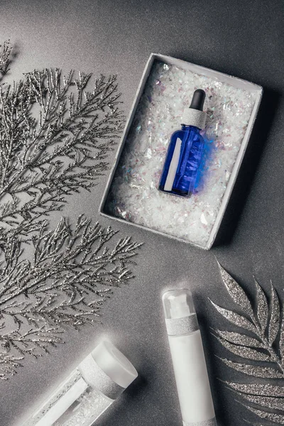 Elevated view of christmas gift box with serum, lotion, micellar water, decorated branches on silver — Stock Photo
