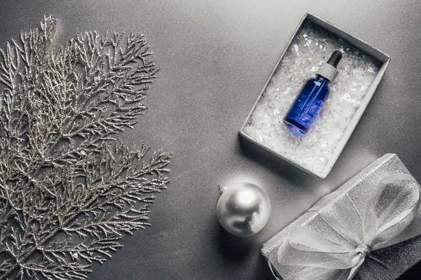Blick von oben auf Serum in Geschenkbox und Weihnachtskugel mit Tannenzweigen auf Silber — Stockfoto