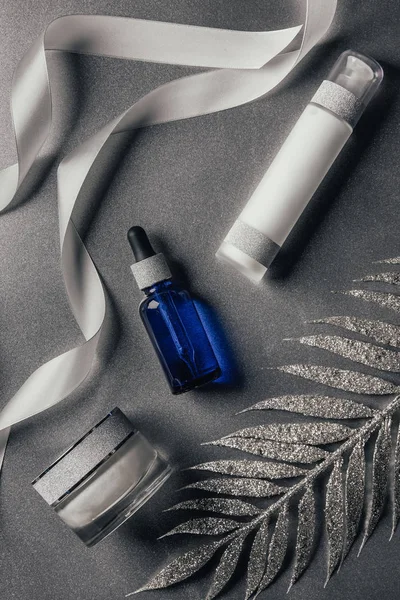 Vue surélevée de lotion, crème de beauté, sérum et ruban avec branche décorée sur argent — Photo de stock