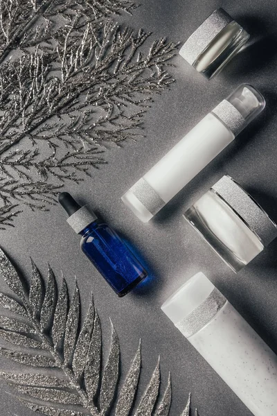 View from above of beauty cream, serum and lotion with decorated branches on silver — Stock Photo