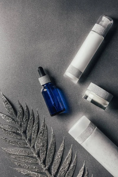 Plat avec crème de beauté, sérum et lotion avec branche décorée sur argent — Photo de stock