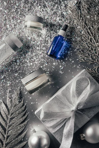 Vista elevada de la composición con crema de belleza, suero, agua micelar y decoraciones navideñas en plata - foto de stock