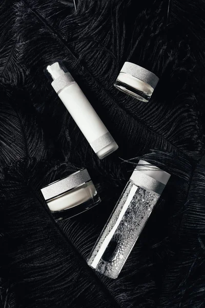 Vue du dessus de la crème de beauté, de l'eau micellaire et de la lotion à la surface avec des plumes noires — Photo de stock