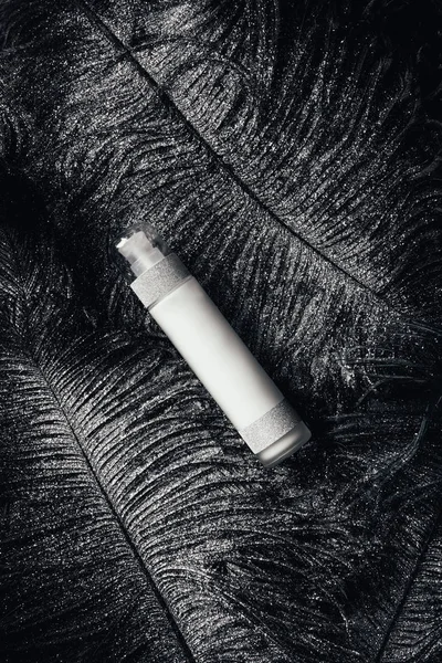 Vue de dessus de la lotion beauté sur la surface avec des plumes noires recouvertes d'argent — Photo de stock