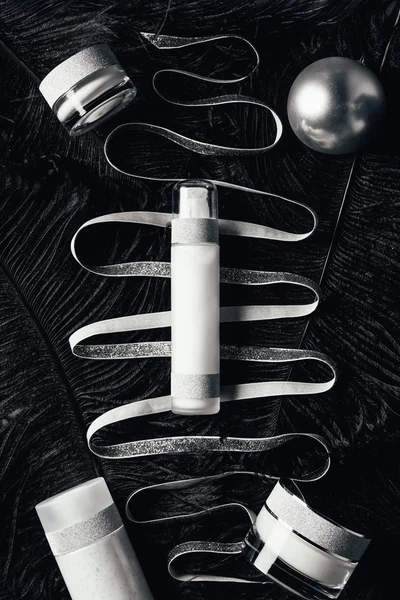 Elevated view of silver christmas ball, beauty treatment equipment, ribbon on surface with black feathers — Stock Photo