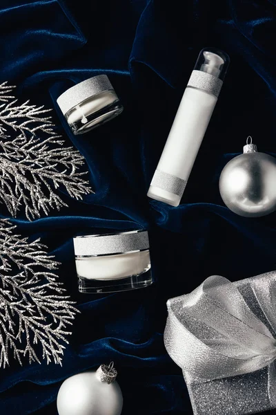 Elevated view of gift box, beauty cream, lotion and silver christmas balls on velvet surface — Stock Photo