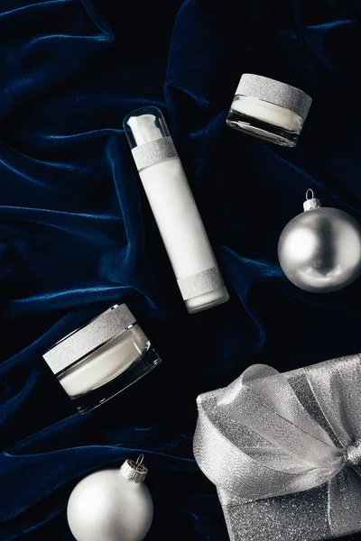 Vue du dessus de la boîte cadeau, crème de beauté, lotion et boules de Noël en argent sur la surface de velours — Photo de stock