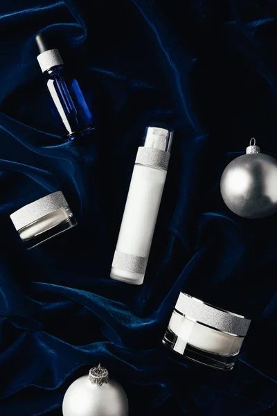 Flache Lage mit Schönheitscreme, Serum, Lotion und silbernen Weihnachtskugeln auf Samtoberfläche — Stockfoto