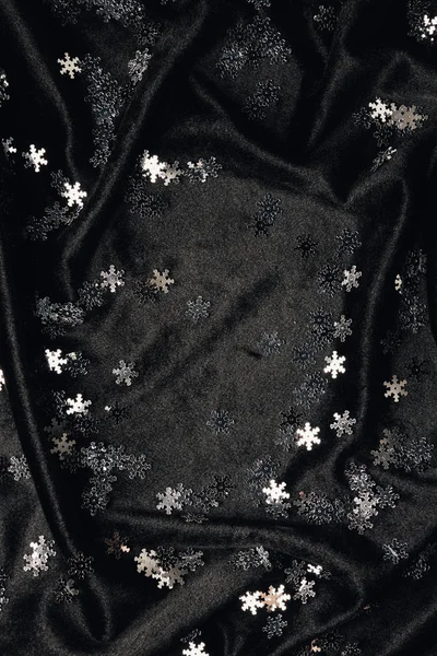 Sfondo festivo con scintillanti fiocchi di neve decorativi d'argento su tessuto nero — Foto stock
