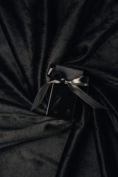 Top view of black perfume bottle with ribbon and bow on black fabric — Stock Photo