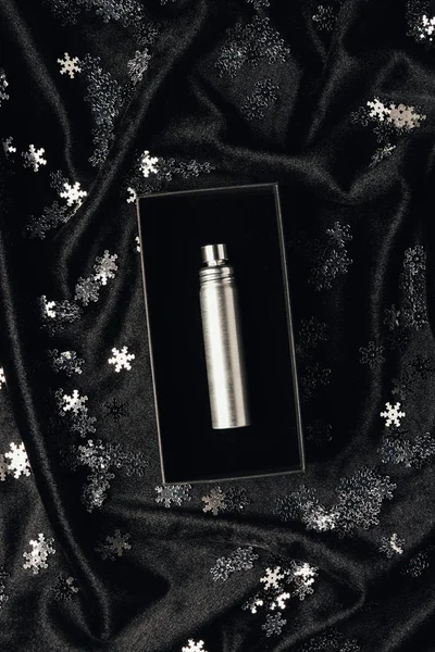 Bouteille de parfum argent en boîte et flocons de neige décoratifs brillants sur tissu noir — Photo de stock