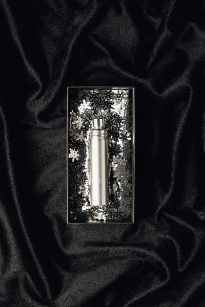 Top view of perfume in box with shiny silver decorative snowflakes on black fabric — Stock Photo