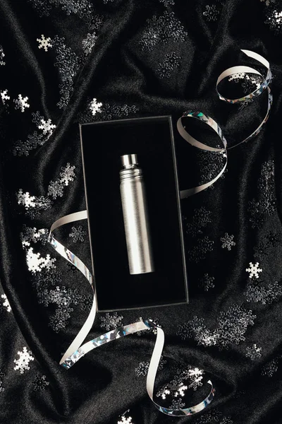 Top view of perfume in box, silver ribbon and shiny decorative snowflakes on black fabric — Stock Photo