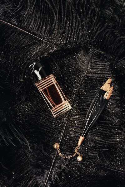 Top view of perfume bottle and decorative black feathers with golden dust — Stock Photo