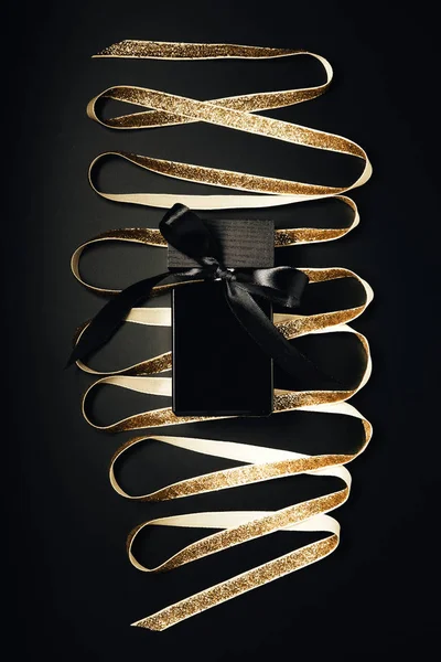 Black perfume bottle with bow and shiny golden ribbon on black — Stock Photo