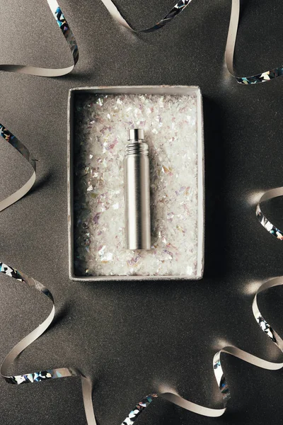 Top view of perfume bottle in box and shiny silver ribbons on grey — Stock Photo