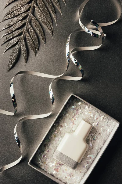 Parfümflasche im Karton, silberne Bänder und glänzende Zierblätter auf grau — Stockfoto