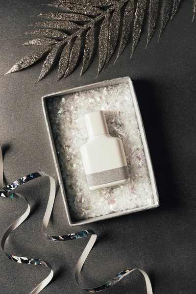 Top view of perfume bottle in box, silver ribbons and shiny decorative leaves on grey — Stock Photo